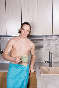 Young sexy guy in the kitchen is drinking coffee.