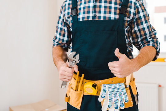 cropped view of handyman holding wrench and showing thumb up