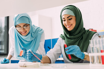 smiling female muslim scientists in hijab with test tube and pipette during experiment in chemical lab