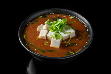Hot miso soup with seaweed, tofu in bowl on black background. Japanese food.