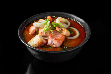 Hot miso soup with salmon, squids, scallops, seaweed, mushrooms, herbs in bowl on black background. Japanese food.