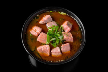 Hot miso soup withsalmon, seaweed, mushrooms, herbs in bowl on black background. Japanese food.