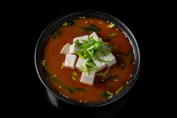 Hot miso soup with seaweed, tofu in bowl on black background. Japanese food.