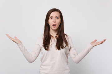 Portrait of shocked concerned young woman in light clothes spreading and pointing hands aside...