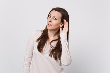 Portrait of concerned young woman in light clothes looking camera and eavesdrop with hearing...