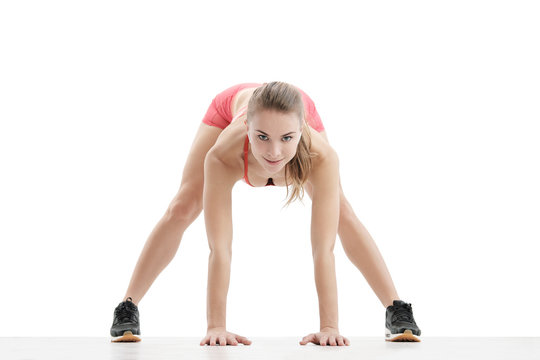 Young athletic woman with an athletic body, wearing wireless headphones and red sportswear stretched over a white background, isolated.