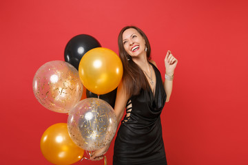 Naklejka premium Smiling young girl in little black dress celebrating looking up holding air balloons isolated on bright red background. International Women's Day, Happy New Year birthday mockup holiday party concept.