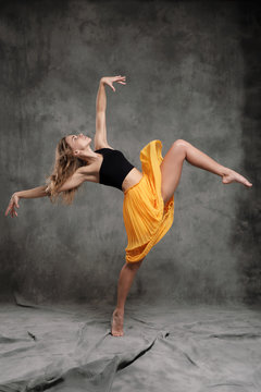 A beautiful graceful slender female dancer performs choreographic figures and movements on a gray dark fabric background.