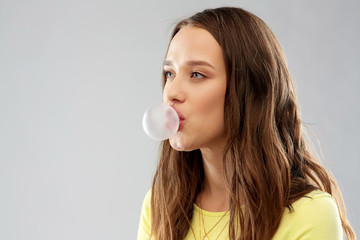 people concept - portrait of young woman or teenage girl blowing bubble gum over grey background