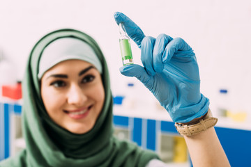 smiling female muslim scientist holding glass ampoule in laboratory