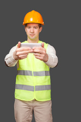 the man in a helmet with phone, in a vest looks in phone