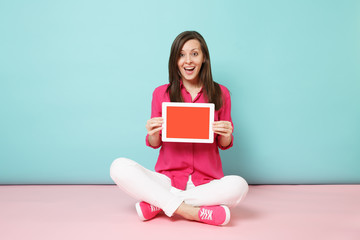 Full length portrait woman in rose shirt blouse, white pants sitting on floor hold tablet pc isolated on bright pink blue pastel wall background studio. Fashion lifestyle concept. Mock up copy space.