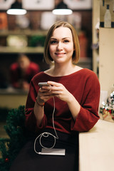 Photo of blonde seller with phone in hands, in black apron on blurred background.