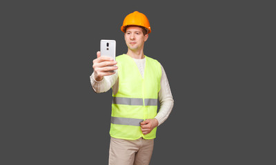 the man in a helmet with phone, in a vest looks in phone