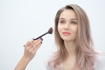 Fototapeta premium Make-up artist makes makeup beautiful blonde girl on a white background. Close-up hands with brush and face.