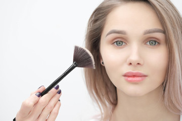 Make-up artist makes makeup beautiful blonde girl on a white background. Close-up hands with brush and face.