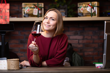 Photo of woman seller with wine glass standing behind cash register