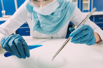 cropped view of female muslim scientist holding test tube with tweezers and experimenting with dry ice in laboratory