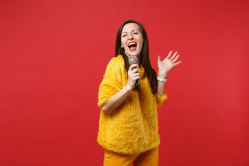 Pretty funny young woman in yellow fur sweater spreading hands sing song in microphone isolated on...