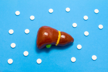 3D anatomical model of liver is on blue background surrounded by white pills as ornament polka dots. Medical concept by pharmacological tableted treating of liver disease, pharmacotherapy chemotherapy