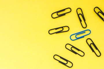 One blue clip and many black clips on yellow uniform background view from above with clear area of half of photo for labels or headers. Concept photo to highlight, not to be like at all