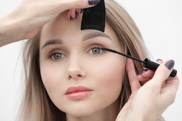 Make-up artist paints a girl with black mascara eyelashes closeup.
