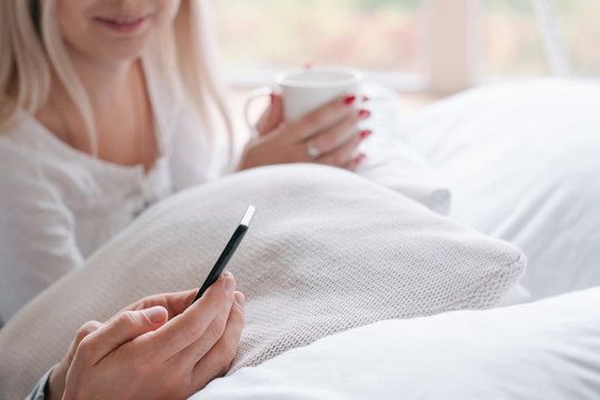 Morning Wake Up Ritual. Young Couple In Bed With Drink And Smartphone.