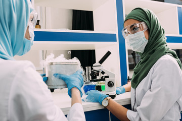 female muslim scientists experimenting with microscope and dry ice in chemical laboratory