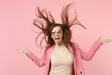 Portrait of crazy young woman in heart glasses showing tongue jumping with flying hair isolated on...