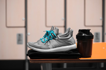 Close up of sports shoes, sportswear and sport water bottle in gym locker room.