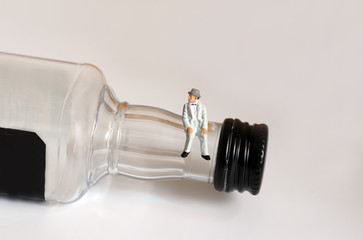 A miniature old man sitting on a liquor bottle.