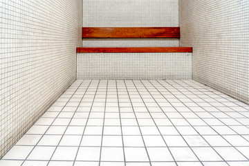 The very sober interior of a prison cell: bare tiled walls and a wooden bench.