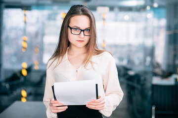 Corporate executive portrait. Office workspace. Young confident business manager in glasses standing with documents.