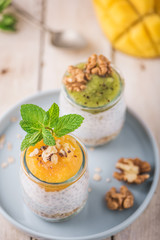 Top view of Homemade pudding of Chia seeds and almond milk with cereals and puree of mango and kiwi with walnuts and mint in glass jars. Vegan healthy morning breakfast or superfood dessert
