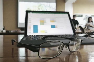 Tired and worn out in a meeting presentation. Glasses in front of a personal computer notebook. blurred data on monitor and people presenting in the backgrounds.