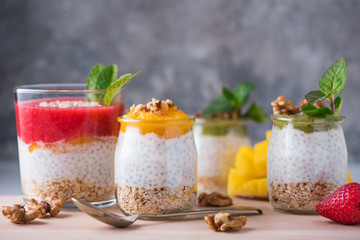 Homemade pudding of Chia seeds and almond milk with cereals and puree of kiwi, strawberry and mango with walnuts and mint in glass jars. Vegan healthy morning breakfast or superfood dessert