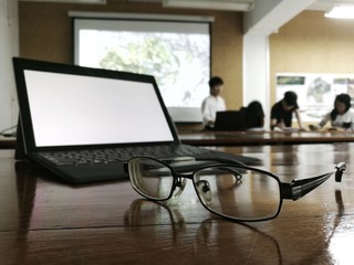 Tired and worn out in a meeting presentation. Glasses in front of a personal computer notebook. blurred white page mock up monitor and people presenting in the backgrounds.