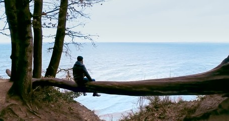 Man sitting by the sea on a tree. Natural scenic view. Admiring nature.
