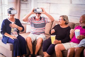 Group of aged old friends have fun at home with vr goggled headset and pop corn - party celebrating time with laughs and friendship for caucasian mature people