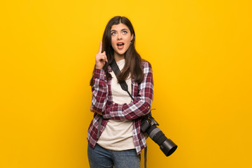 Photographer teenager girl over yellow wall thinking an idea pointing the finger up