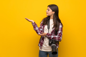 Photographer teenager girl over yellow wall extending hands to the side for inviting to come
