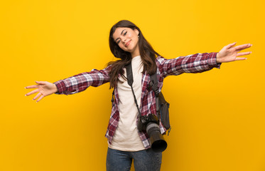 Fototapeta na wymiar Photographer teenager girl over yellow wall presenting and inviting to come with hand