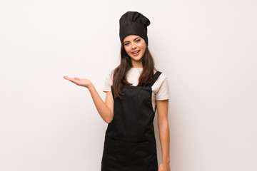 Teenager chef  over white wall holding copyspace imaginary on the palm to insert an ad