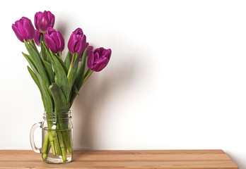 Purple tulips in a glass jar standing on the wooden table