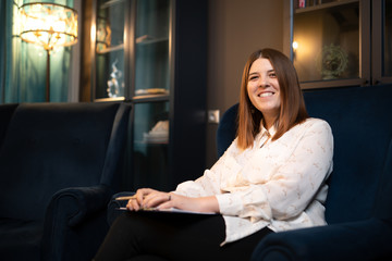 Image of smiling woman psychologist in white shirt sitting on blue chair.