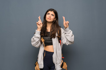 Teenager traveler girl over wall with fingers crossing and wishing the best