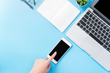 A woman is holding a smartphone isolated with a minimal blue desk, concept of online shopping payment, internet work at home, e-commerce, copy space, flat lay, top view, mock up