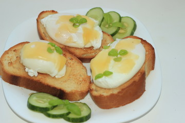 Poached eggs on toasted baguette slices.with a cucumber on a white plate