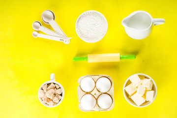 Fototapeta na wymiar Baking ingredients and tools on trendy bright yellow background - flour, eggs, sugar, milk, butter, layout, flatlay top view copy space banner