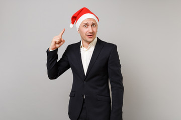 Puzzled young business man pointing index finger on Christmas hat on head isolated on grey wall background. Achievement career wealth business. Happy New Year 2019 celebration holiday party concept.